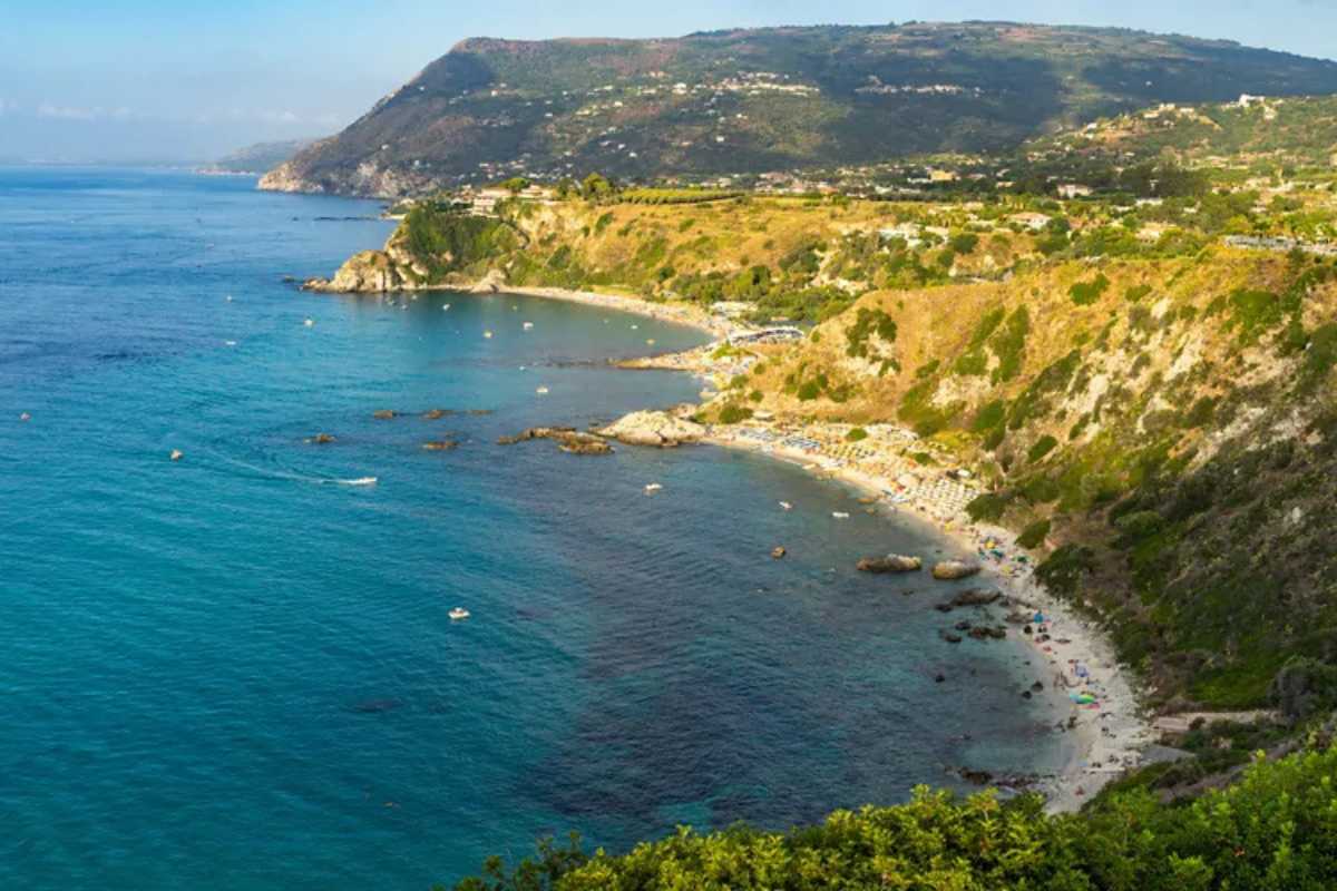 Vista panoramica con scogliere di granito, mare turchese e faro di Capovaticano al tramonto, atmosfera suggestiva e rilassata
